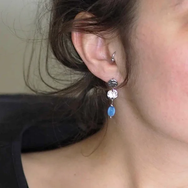 zoom sur l'oreille d'une femme portant une paire de boucles d'oreilles argentées upcyclées avec des petites perles bleues
