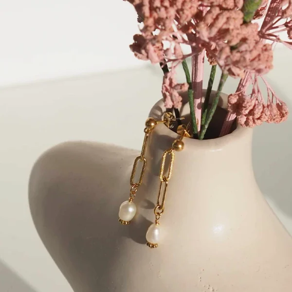 Une paire de boucles d'oreilles upcyclée dorée et blanche accrochée au bord d'un vase avec des fleurs