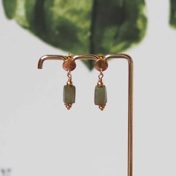 Une paire de boucles d'oreilles dorée avec des pierres rectangulaires vertes de seconde main sur un portant