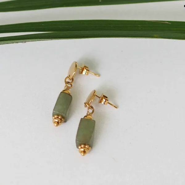 Une paire de boucles d'oreilles upcyclées verte et dorée à plat sur fond blanc