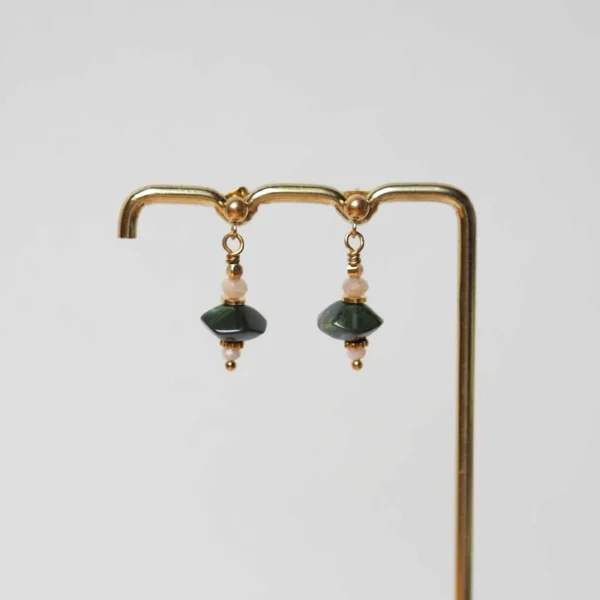 une paire de boucles d'oreilles upcyclée composée de perles kaki de seconde main et de petites perles rose pâle sur un portant