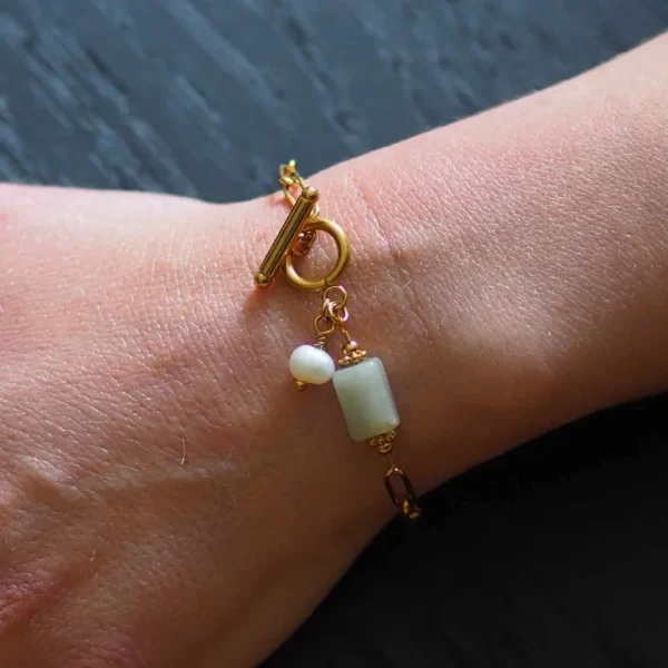 zoom sur un poignet de femme qui porte un bracelet doré composé d'une chaîne en acier inoxydable et de pierres et perles naturelles de seconde main