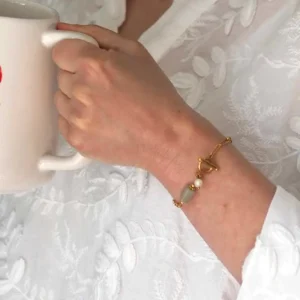 une femme tenant une tasse à la main avec au poignet un bracelet upcyclé doré avec des perles naturelles de seconde main