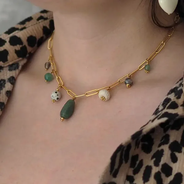 un cou de femme portant un collier upcyclé avec une chaîne en acier inoxydable dorée et sept pierres et perles vertes et écrues montées en breloques