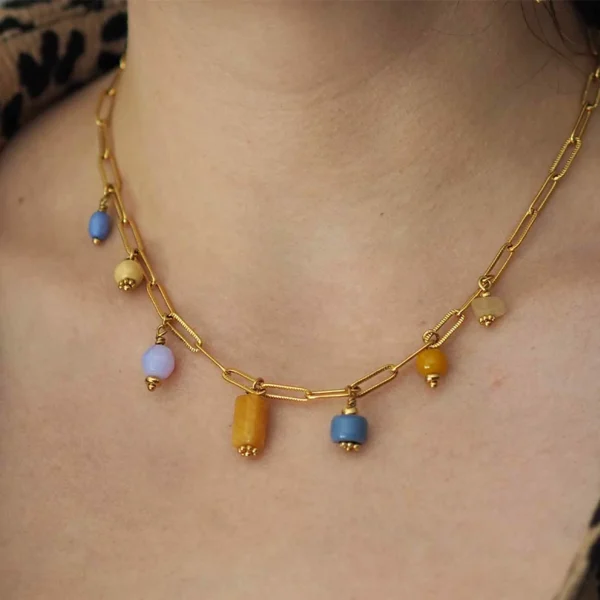 un cou de femme portant un collier upcyclé avec une chaîne en acier inoxydable dorée et des perles oranges et violettes de seconde main montées en breloques