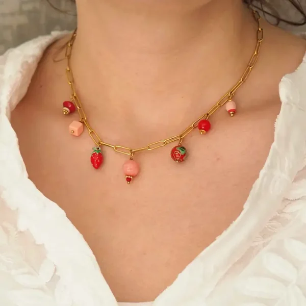 un cou de femme portant un collier upcyclé fantaisie avec une chaîne en acier inoxydable dorée et sept perles rouges et roses de seconde main montées en breloques