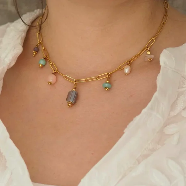 un cou de femme portant un collier upcyclé avec une chaîne en acier inoxydable dorée et sept perles dans les tons pastel montées en breloques