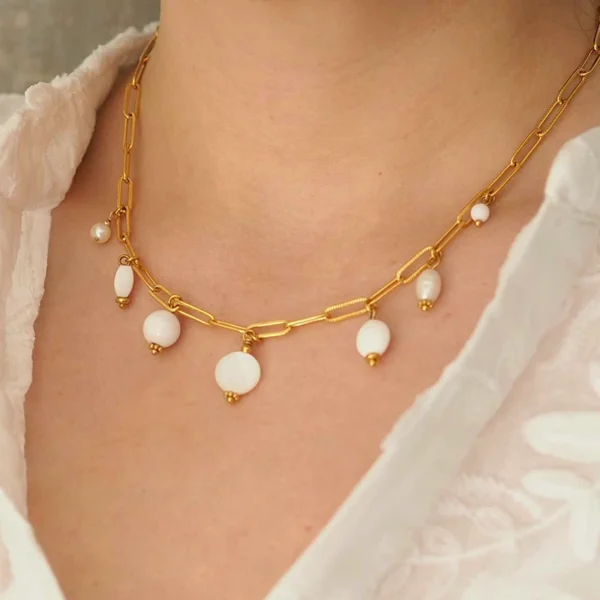 Un cou de femme portant un collier upcyclé avec une chaîne en acier inoxydable dorée et sept perles blanches montées en breloques