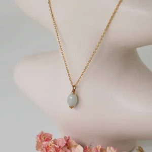 collier upcyclé avec une chaîne fine dorée et un pendentif en pierre de seconde main posé sur un vase beige